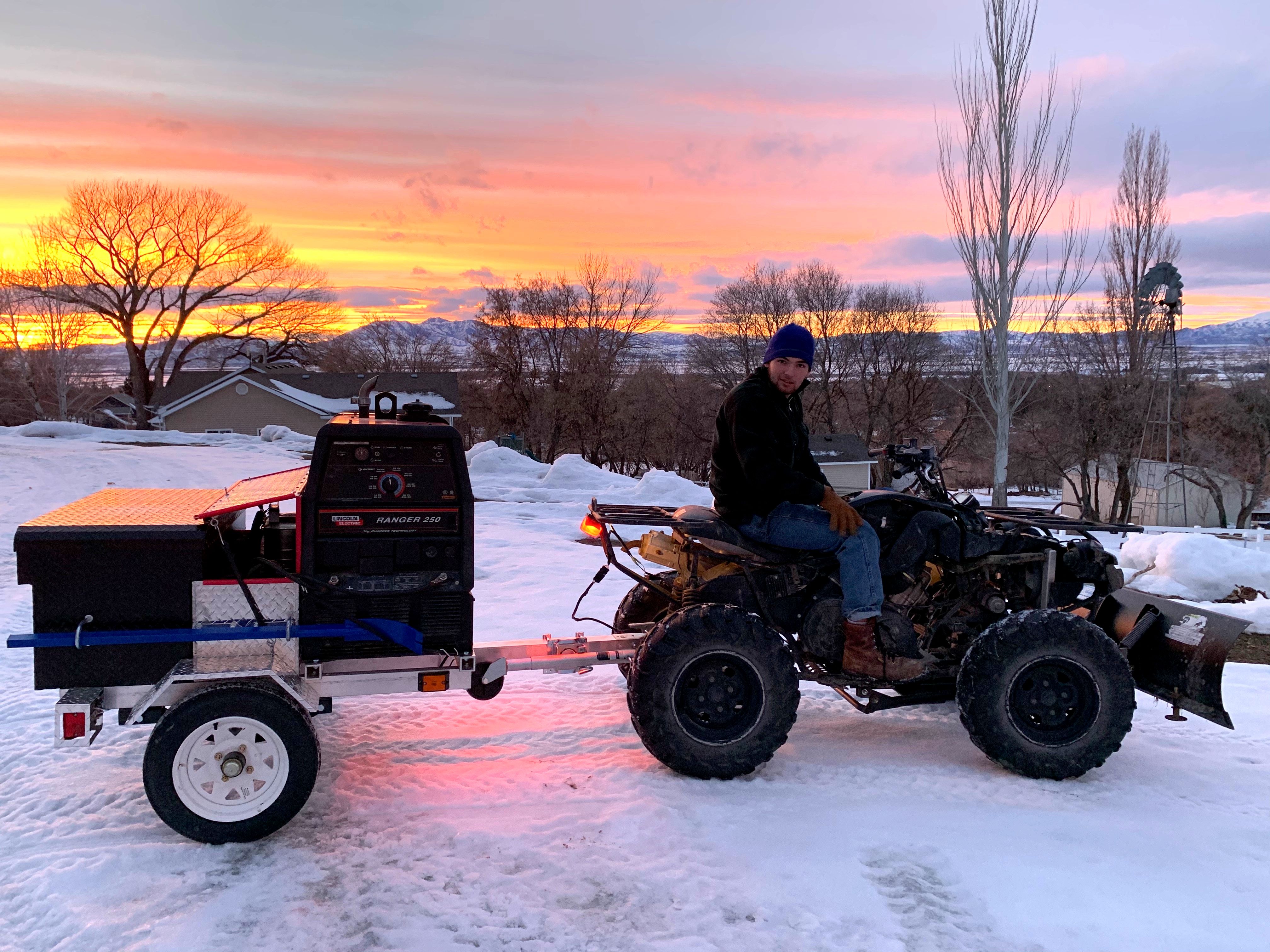 Jimmie on his ATV Frank(enstein) towing his brand-new portable engine-driven welder Abe (it's a Lincoln) at sunset in the snow.