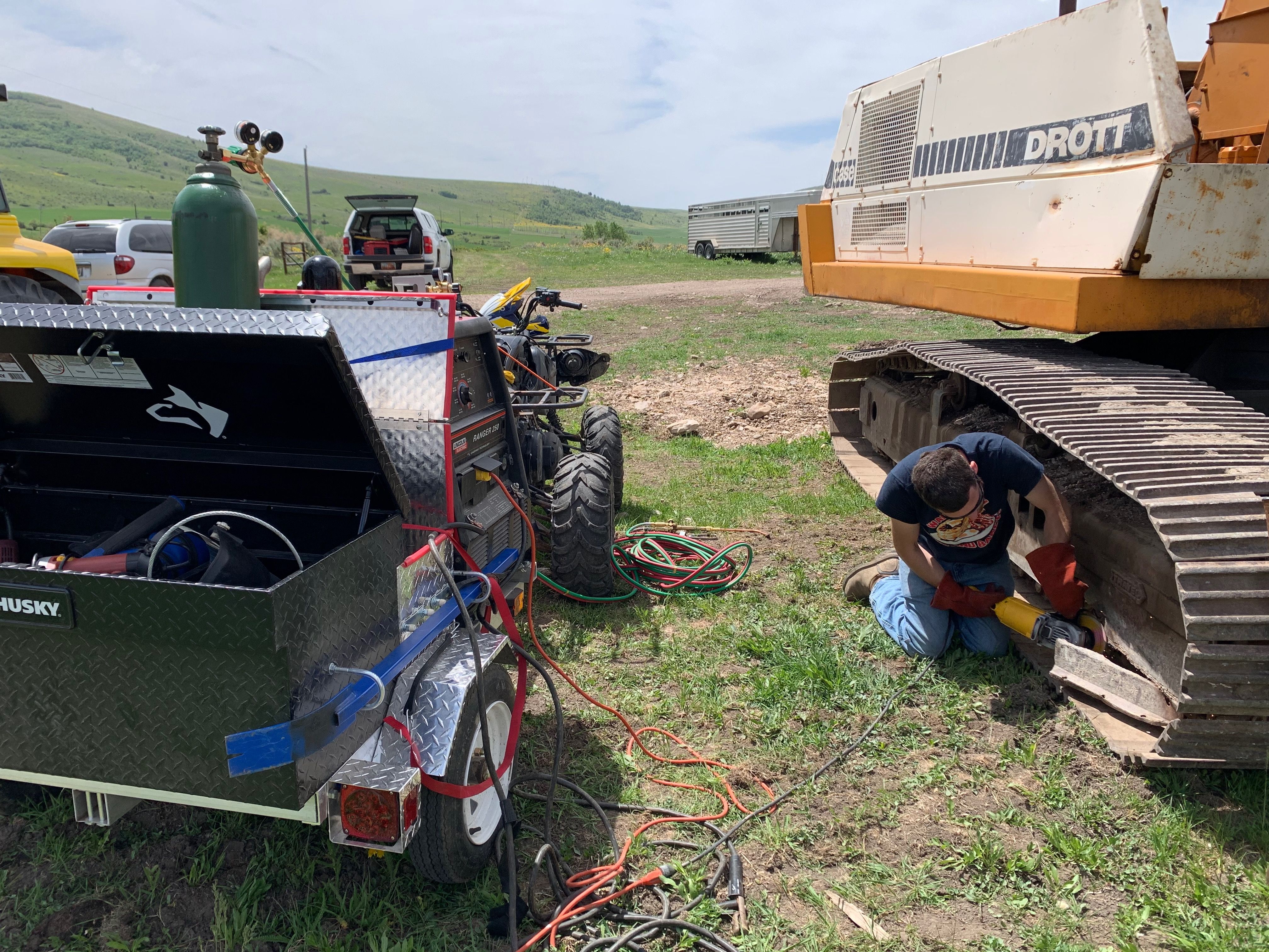 Jimmie grinding on a repair to the tracks of a large excavator in a grassy field on a farm.