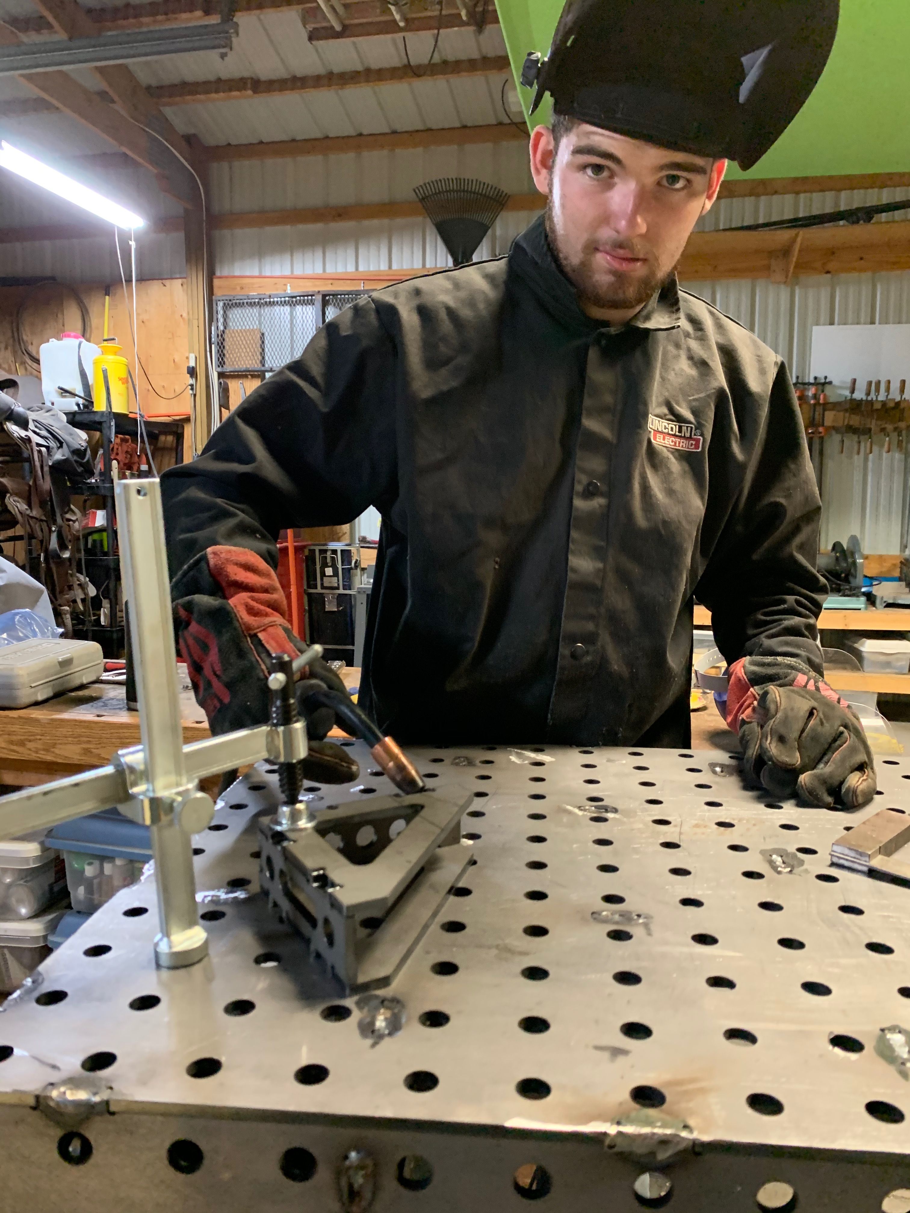 Jimmie in his welding gear, standing at his fabrication table with his MIG welder in-hand.
